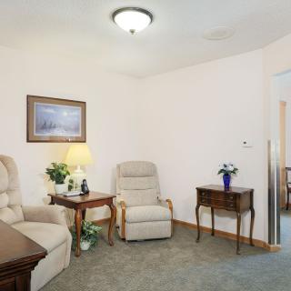 A cozy living room with comfortable armchairs, a side table with a lamp, and decorative flowers.