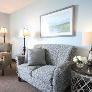 A cozy living room with patterned sofas, elegant lamps, and a landscape painting.