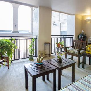 A well-decorated balcony featuring wooden furniture and green plants, creating a cozy outdoor seating area.