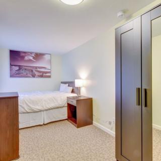 A cozy bedroom featuring a bed, wardrobe, and bedside lamp, with artwork on the wall.