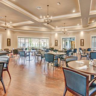A spacious and elegantly designed restaurant dining area with well-arranged tables and chairs under bright chandeliers.