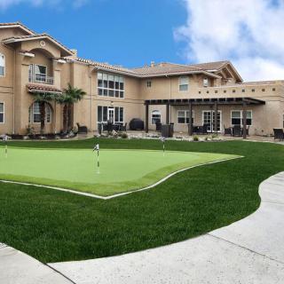 A luxurious mansion with a well-maintained lawn and a putting green in the backyard.