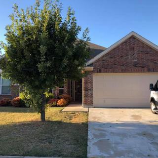 A suburban brick house with a driveway and a tree in the front yard.