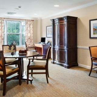 A well-furnished living room with a table and chairs near a window, featuring a large cabinet and a computer desk.