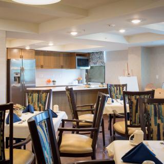 A well-lit dining area with tables and chairs arranged near an open kitchen.