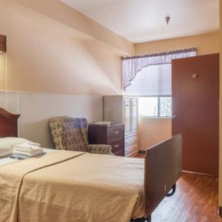 A simple hospital room with a bed, chair, and wardrobe.