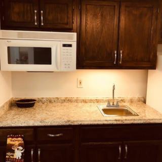 A small kitchen area with a microwave, dark wooden cabinets, and a granite countertop featuring a sink.