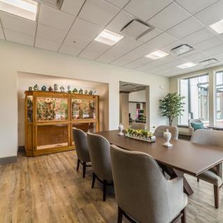 A well-lit dining room with a table and chairs, featuring a wooden cabinet and decorative plants.