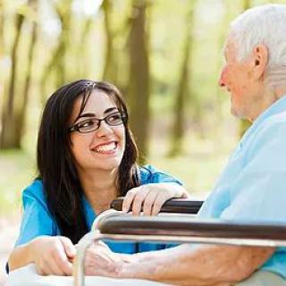 A caregiver smiling and interacting with an elderly person outdoors.