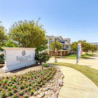 A well-landscaped entrance to an apartment complex with a prominent sign and manicured gardens.