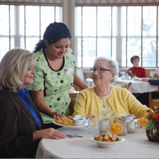 A waitress serves food to two elderly women dining together in a restaurant setting.