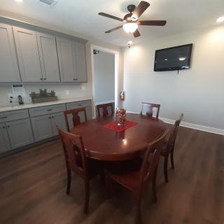 A dining area with a wooden table and chairs, equipped with a ceiling fan and wall-mounted television.
