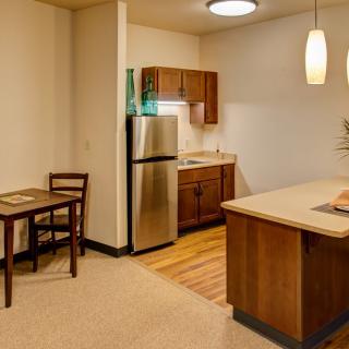 A modern apartment kitchen with an open layout featuring stainless steel appliances and wood cabinetry.