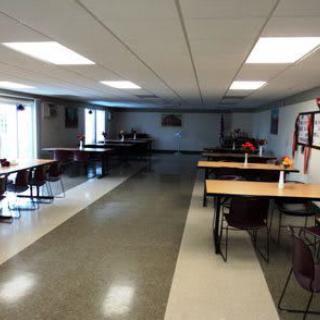 An empty cafeteria with tables and chairs arranged neatly under bright overhead lighting.