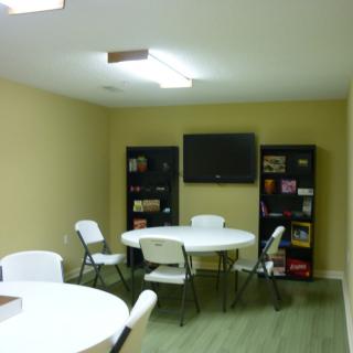 A small meeting room with tables, chairs, a TV, and bookshelves filled with games.