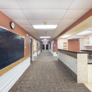 A well-lit hallway featuring carpeted flooring and a chalkboard, leading to various rooms.
