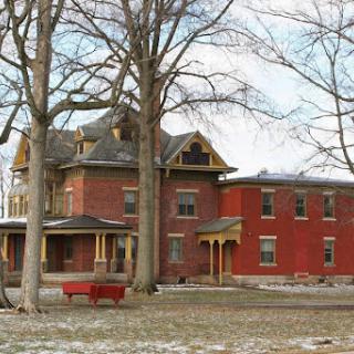 A historic red brick mansion surrounded by trees, showcasing elegant architectural details.