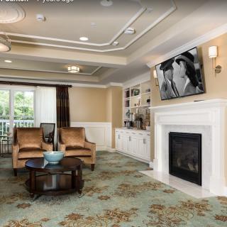 A cozy living room with elegant armchairs, a fireplace, and a television mounted above.