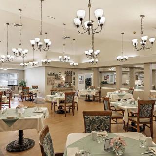 A well-lit dining area with multiple tables set for a meal, featuring elegant chandeliers.