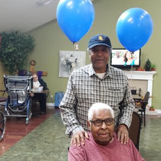 A warm moment shared between family members in a care facility, celebrating with blue balloons.