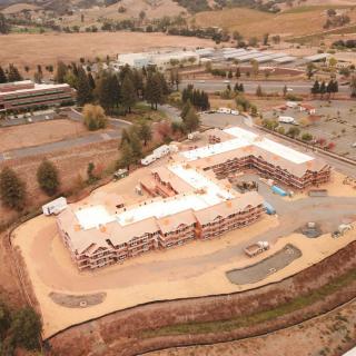 Aerial view of a construction site with an L-shaped building under development surrounded by hills.
