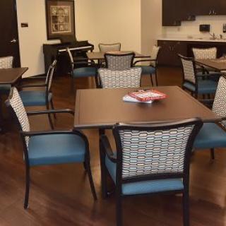 A cozy communal dining area with several tables and chairs, featuring a kitchenette in the background.