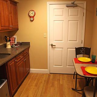 A cozy kitchen with wooden cabinets, a small dining table set for two, and a wall clock.
