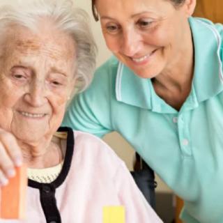 A caregiver assisting an elderly woman with a playful activity.