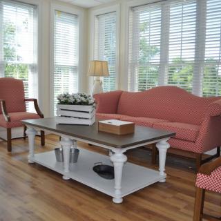 A cozy living room with pink sofas and armchairs, a white coffee table, and large windows letting in natural light.