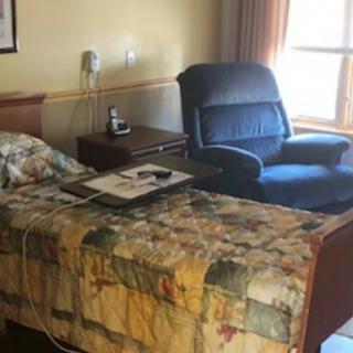 A cozy bedroom with a quilted bed and a comfortable armchair by the window.