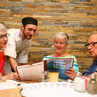 A group of elderly people reviewing a menu with a waiter in a restaurant.