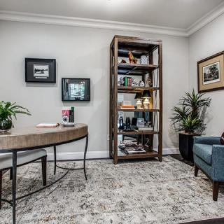 A cozy office space featuring a desk, bookshelf, armchair, and decorative plants.