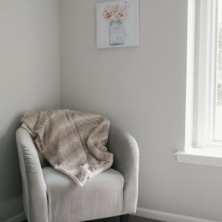 A cozy corner with a cushioned chair, draped blanket, and soft natural light.