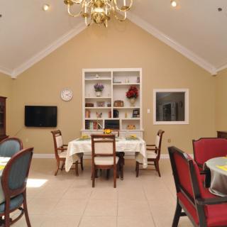 A cozy dining room with a chandelier, elegant chairs, and a neatly organized bookshelf.