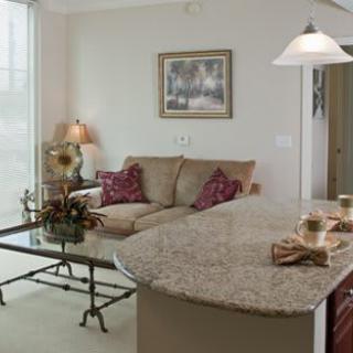 A cozy living room with a beige sofa, glass coffee table, and adjacent kitchen counter.
