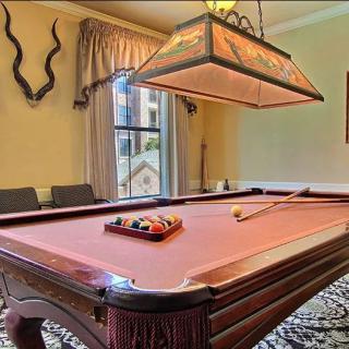 A well-decorated game room featuring a billiards table with a cue stick and balls arranged, illuminated by an overhead light.