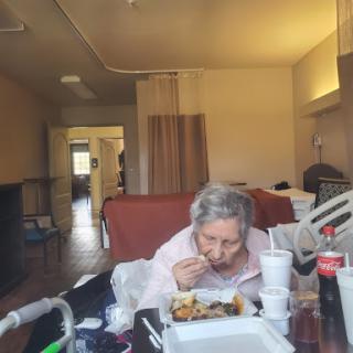 An elderly woman enjoying a meal in a cozy care facility setting.