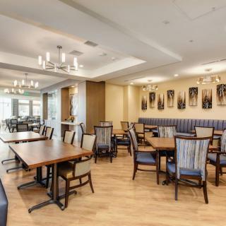 A spacious and elegantly designed dining area with wooden tables, cushioned chairs, and decorative chandeliers.