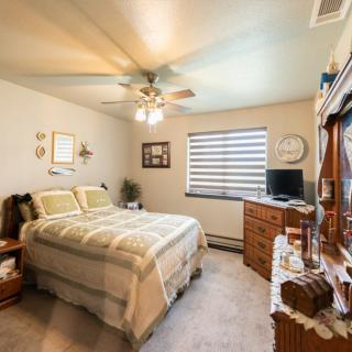 A cozy bedroom interior with neatly arranged furniture and a ceiling fan.