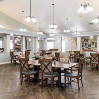 A spacious and modern dining area with wooden floors, round tables, and stylish chairs, illuminated by multiple hanging light fixtures.