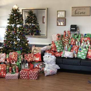 A festive living room with a decorated Christmas tree and a sofa piled high with colorful wrapped presents.