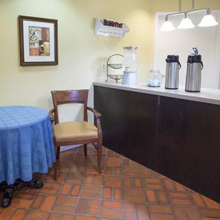 A small beverage area with a coffee station and a table with a chair.
