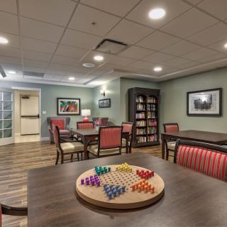 A cozy indoor game room with a Chinese checkers board on the table, surrounded by chairs and bookshelves.