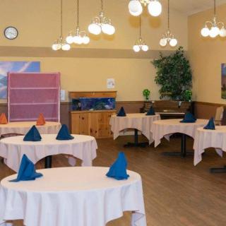 An empty restaurant dining room with round tables adorned with white tablecloths and folded napkins.