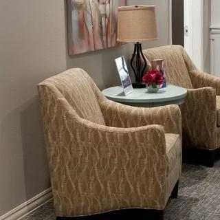 A cozy seating area with two patterned chairs, a side table with a lamp, and decorative elements.
