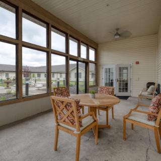 A cozy patio area with a round table and chairs, featuring large windows providing an outdoor view.