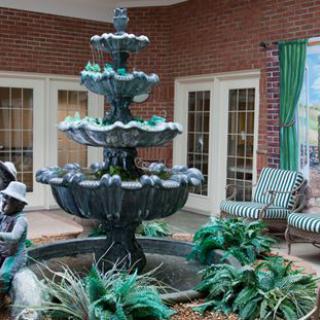 An indoor garden scene featuring a tiered fountain surrounded by lush plants and seating.