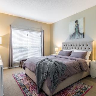 A cozy bedroom with a neatly made bed, featuring a tufted headboard and decorative artwork on the wall.
