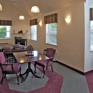 A cozy dining room with a table and chairs, featuring large windows and warm lighting.