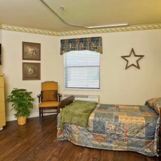 A cozy bedroom featuring a bed with a patterned quilt, a comfortable chair, and decorative wall art.